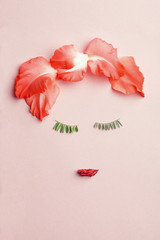 Woman face made of green leaves as eyelashes and red flower petals as lips and hair. Beauty concept, flat lay