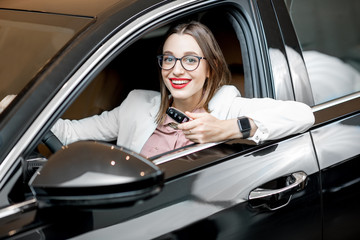 Portrait of a happy owner sitting with keychain on a driver seat of a new luxury car at the showroom