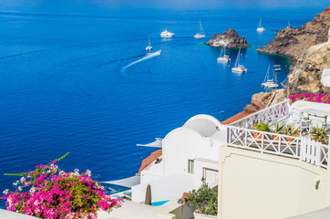 Oia Village, Santorini Cyclade islands, Greece. Beautiful view of the town with white buildings, blue church\'s roofs and many colored flowers