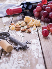 Red wine bottle, fresh grape, cheese, almond nuts on a wooden background with copy space.