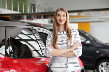 Young woman near new car in modern auto dealership