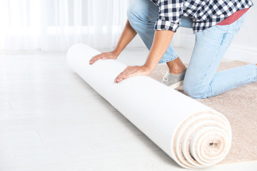 Man rolling out new carpet flooring indoors, closeup. Space for text