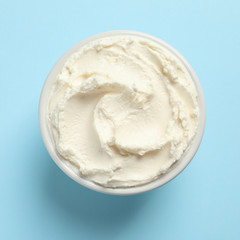 Bowl of tasty cream cheese on color background, top view