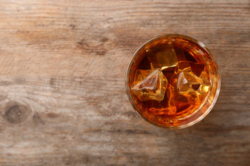 Golden whiskey in glass with ice cubes on wooden table, top view. Space for text