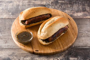 Choripan. Traditional Argentina sandwich with chorizo and chimichurri sauce on wooden table