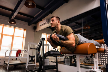 Fototapeta na wymiar Young sportive man does hyperextension exercise in gym