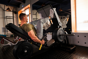 Young sporty man does leg exercises in gym side view