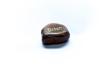 A brown polished river stone, over white with the word dream written on it. Not isolated