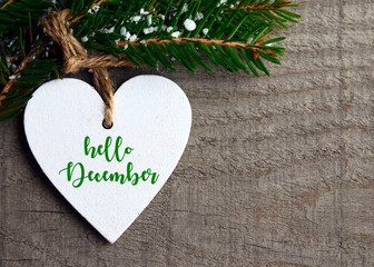 Hello December.Decorative white wooden Christmas heart and fir tree branch on old wooden background.Winter holidays concept with space for text.Selective focus.
