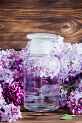 Fresh lilac flower petals floating on water in a glass jar on a dark wooden background