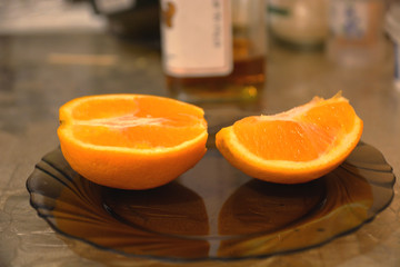 Orange on the plate with reflection and blured bottle of whiskey on the table background.