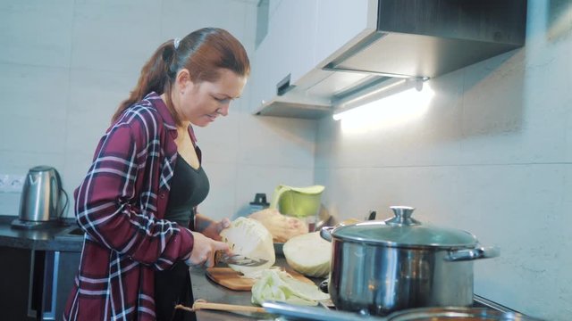 woman in the kitchen preparing a meal concept. girl in the kitchen cuts cabbage with a knife. lifestyle cook vegetarian food healthy food. girl at home in the kitchen slow motion video