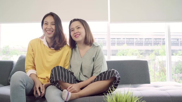 Lesbian Asian couple watching TV laugh in living room at home, sweet couple enjoy funny moment while lying on the sofa when relax at home. Lifestyle couple relax at home concept.