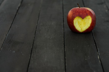 Red apple with a heart cut out on a wooden background