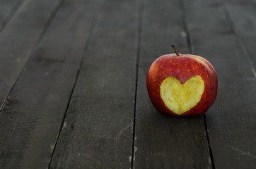 Red apple with a heart cut out on a wooden background