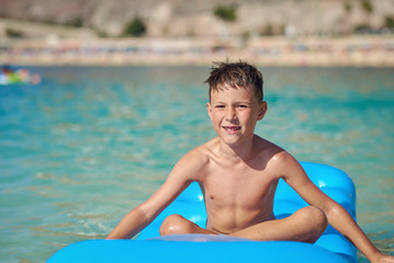 Cute European boy is sitting and swimming on the blue air matress, he is enjoying his holidays and...
