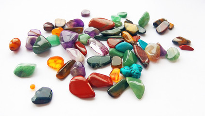Spilling assorted natural bright coloured semi precious gemstones and gems on white background