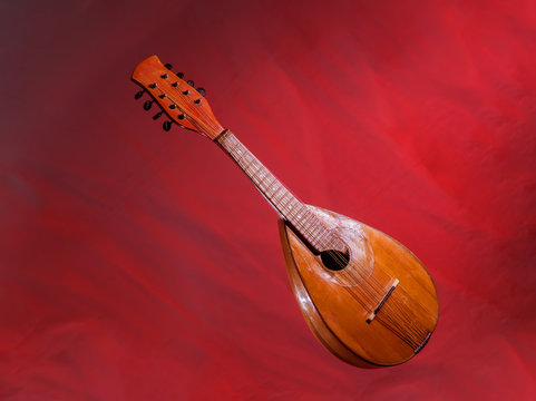 Old mandolin located diagonally on a bright red background. Baroque string musical instrument..