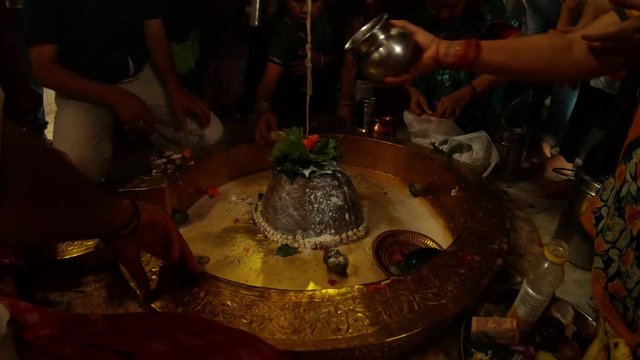 Hands of big crowd of people pour water and milk over swayambhu self-existing lingam and put leaves and flowers in ancient hindu temple Rishikesh