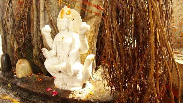 Marble statue of godess Ganga under big banyan tree near lingams hindu temple Rishikesh