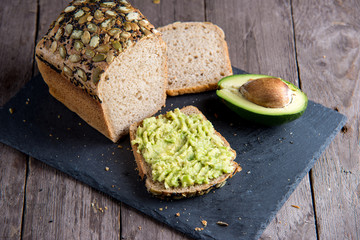 Healthy bread with fresh avocado on stone plate on wooden background.