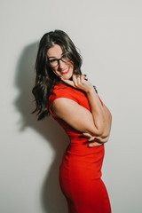 .Young and pretty brunette girl in a red dress and some black glasses. Playful and funny expression. Lifesytle. Beauty.