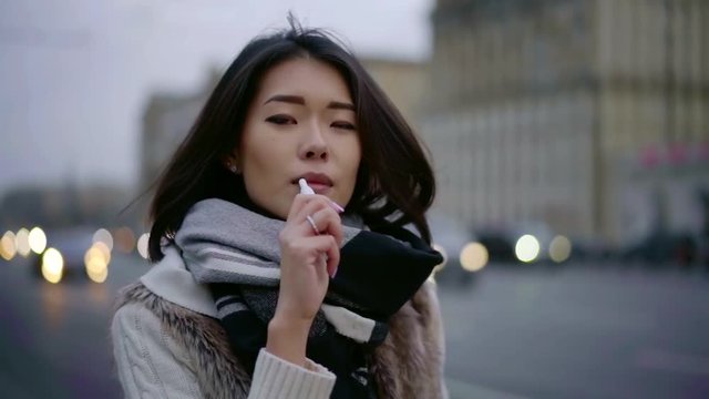 young korean woman is smoking vape outdoors in city in autumn day, close-up of face