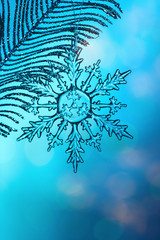 Chrystal transparent glass snowflake on silver branch, blue bokeh background, close up with copy space