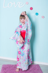 8 years old caucasian girl demonstrates japanese blue pink with flowers kimono, claps her hands, dance  