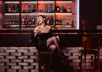 A cheerful beautiful woman wearing a black shiny dress sitting at a bar counter
