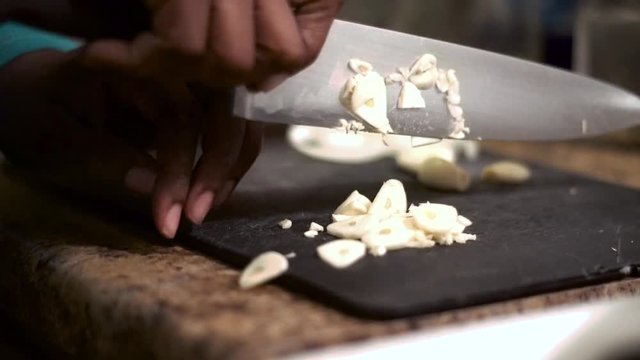 African american black woman is preparing dinner by cutting garlic and onions on the kitchen table.  close up shot of knife dicing the food to small pieces to add to tonight meal