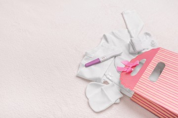 Pregnancy test and baby clothes. Beautiful still life on a plush blanket.