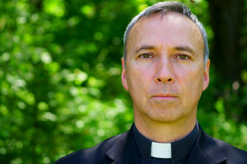 Fototapeta premium A good looking catholic priest is standing in the forest, looking at us, concentrating.