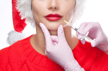The doctor cosmetologist makes injection on the lips of a beautiful woman in the Santa Claus hat....