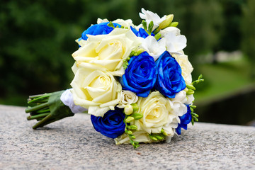 Wedding bouquet from blue and yellow roses on stone texture and tree background