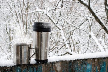 Iron mugs of hot drink on a snow covered terrace.