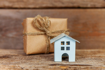Obraz na płótnie Canvas Miniature white toy house and gift box wrapped craft paper on old shabby rustic wooden background. Mortgage property insurance dream home concept. Buying new house for family