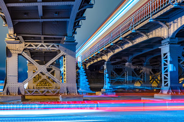 Obraz premium Ruch transportu. Mosty kolejowe. Stary most. Tracer z reflektorów samochodowych. Ruch drogowy. Sankt Petersburg. Światło z przejeżdżającego pojazdu.