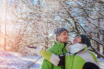 Couple in love throwing snow and hugging in winter forest. Young people having fun