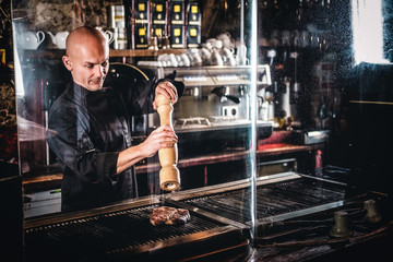 Master chef wearing uniform cooking delicious beef steak on a kitchen in a restaurant