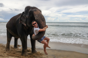 Portrait of a young guy with an elephant on the background of a tropical ocean beach. Elephant hugs...