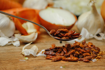 Dried red hot small chilli peppers in spoon and on small ceramic plate. Old wooden table and various of vegetable in the background.