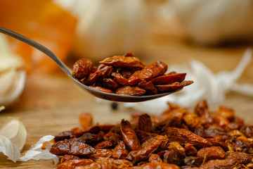 Dried red hot small chilli peppers in spoon and on small ceramic plate. Old wooden table and various of vegetable in the background.