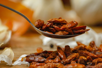 Dried red hot small chilli peppers in spoon and on small ceramic plate. Old wooden table and various of vegetable in the background.