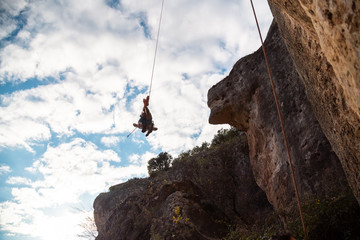 Man in hardhat hanging on rope while doing rappel and showing pirouettes flying in air © pablobenii
