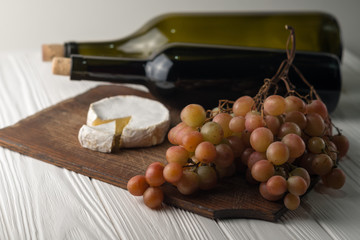 Bottles of wine on a white wooden background with grapes and Camembert cheese