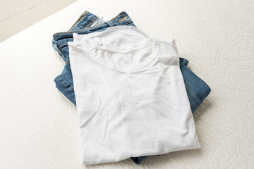 High angle view of folded plain white t-shirt and blue jeans on cream coloured bedding  (selective focus)