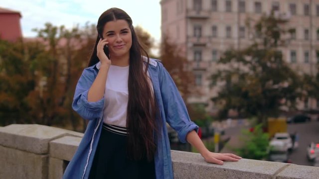 happy young woman has phone conversation outdoors. girl wearing denim t-shirt using smartphone