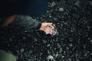 Male hand picks up from ground, black volcanic sand beach melting piece of freshwater ice, part of iceberg or glacier, global warming and climate change threat concept