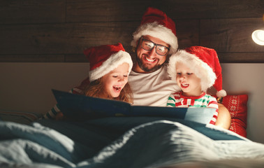 Merry Christmas! family father reads to children book before bed in bed.